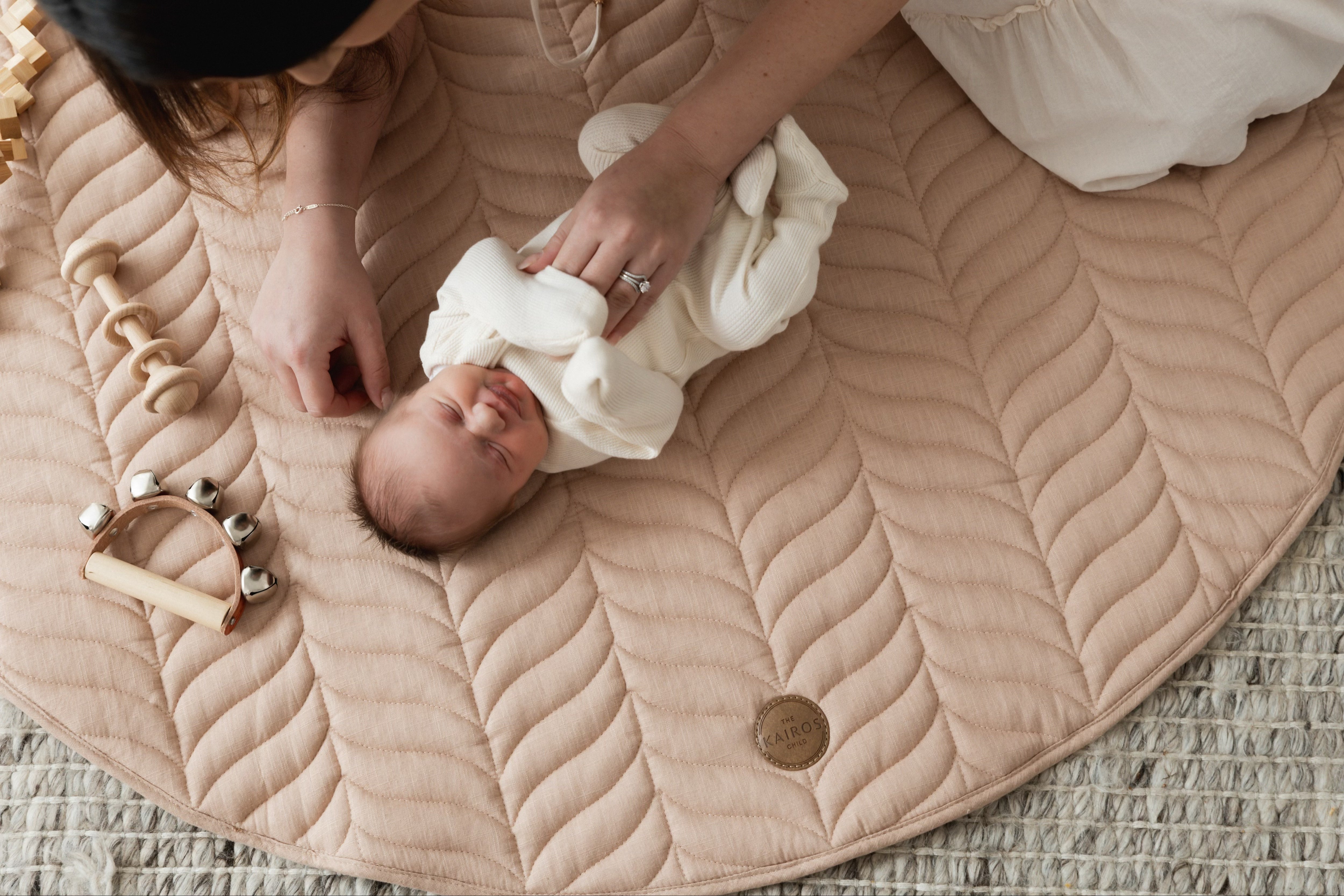 A newborn baby resting on The Kairos Child's Pampas Linen Play Mat with their mother